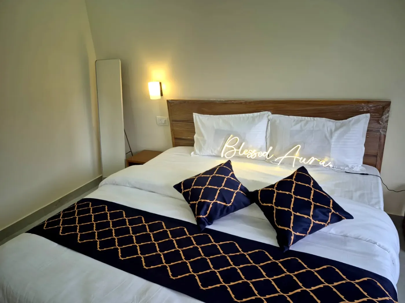 King bed dressed in navy and gold linen beneath a glowing Blessed Aura neon sign